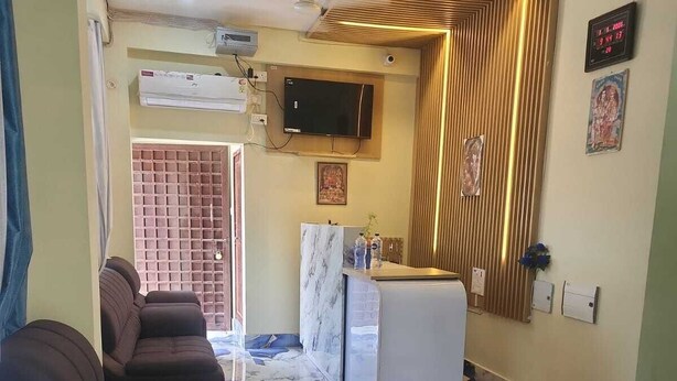 A living room with a sofa, a small table, a marble floor, a TV mounted on the wall, and a kitchen area with a counter and cabinets. - Hotel Navin Palace (Bhagalpur)