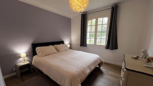 Een slaapkamer met een bed, twee bedlampen, een raam met gordijnen, een dressoir en een kroonluchter.