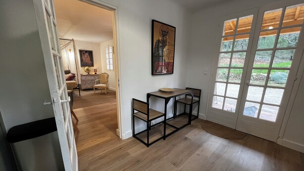 Een kamer met een houten vloer, een eettafel met stoelen, een schilderij aan de muur en een deur naar een buitenruimte.