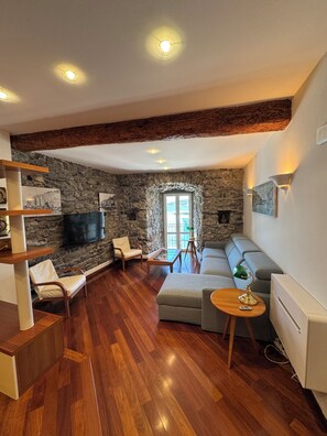 A living room with a stone wall, wooden floor, a sofa, a coffee table, and a television. - Maury's Sea View apartment in the heart of Portovenere - with private garage. (PORTO VENERE)