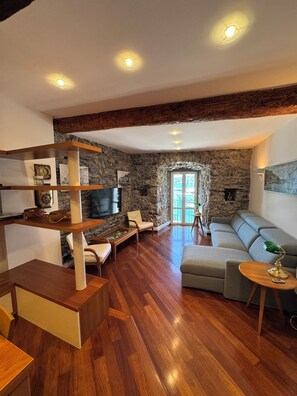 A living room with a stone wall, wooden flooring, a sofa, a TV, and a fireplace. - Maury's Sea View apartment in the heart of Portovenere - with private garage. (PORTO VENERE)