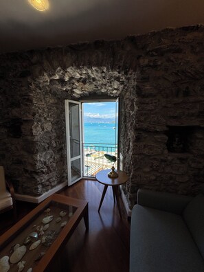 A stone-walled room with a view of the sea, a wooden table, a sofa, and a small round table with a lamp. - Maury's Sea View apartment in the heart of Portovenere - with private garage. (PORTO VENERE)