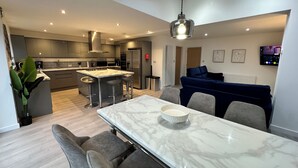Une cuisine moderne avec un îlot central, des tabourets de bar, une table à manger avec des chaises, un canapé et un téléviseur fixé au mur.