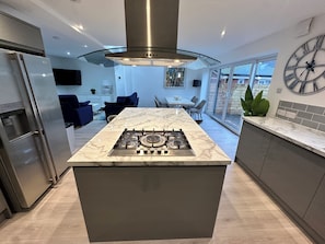 A modern kitchen with a central island, stainless steel appliances, and a large window offering a view of the outdoors.