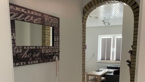 Ein Flur mit einem Spiegel, einem Ziegelbogen und Blick in einen Wohnbereich mit Tisch und Couch.