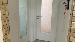 Ein Flur mit zwei Türen, eine mit satiniertem Glas und Schlüsselloch, die andere mit Griff und Schlüsselloch. Der Boden ist Holzboden, und an einer Seite ist eine Ziegelwand.