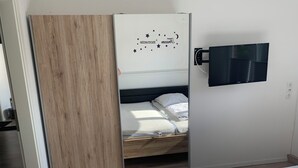 Ein Schlafzimmer mit einem Bett, einem Holzschrank, einem an der Wand montierten Fernseher und einer Deckenleuchte.