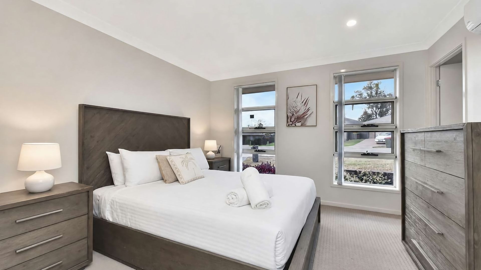 A modern bedroom with a large bed, bedside tables, a dresser, and a window with a view.