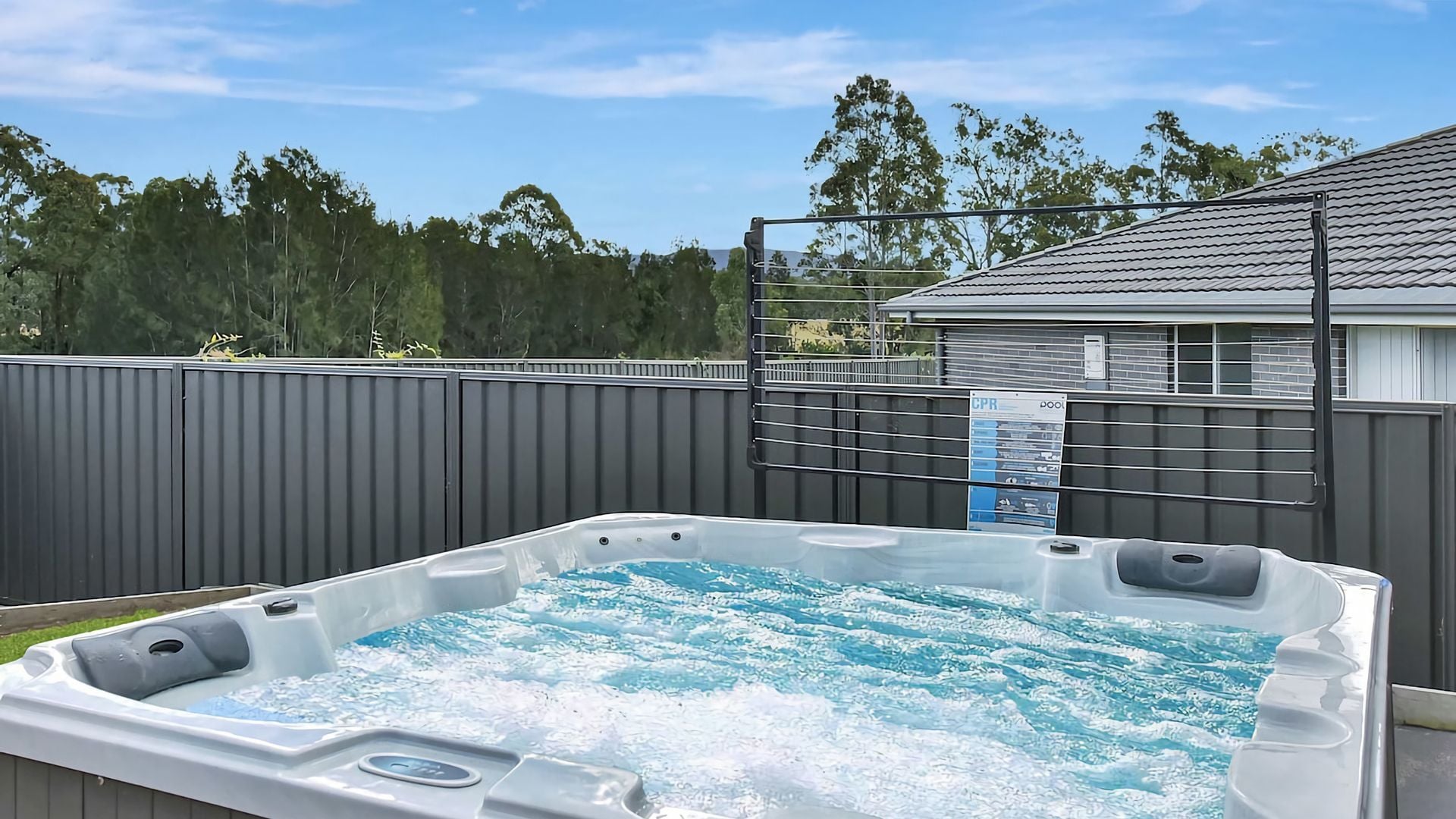 A hot tub with a metal fence and a house in the background.