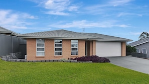 A residential house with a brick facade, a garage, and a well-maintained lawn. - Hunter Hideaway | Pet Friendly, Games Room, Spa (Cessnock)