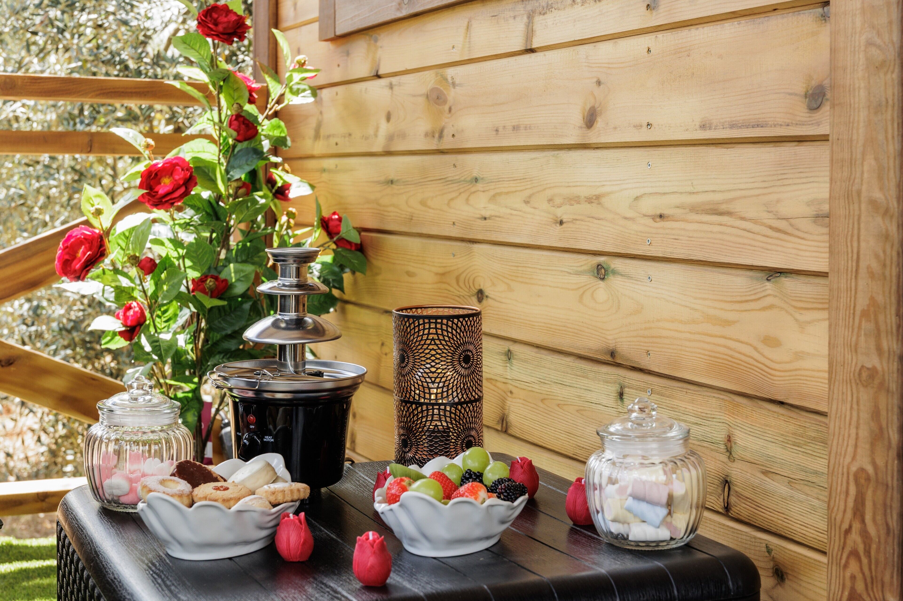Una terraza de madera con una mesa dispuesta con comida, una vela y un arreglo floral.