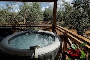 Un jacuzzi al aire libre con una terraza de madera y olivos al fondo.