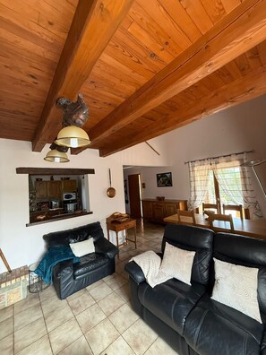 A spacious living area with a high wooden ceiling, a black leather sofa, a dining table, and a kitchen visible through an open doorway. - Chez Polo - House with swimming pool in Vallon-Pont-d'Arc (Vallon-Pont-d'Arc)