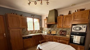 A kitchen with wooden cabinets, a tiled floor, a table with chairs, and a microwave. - Chez Polo - House with swimming pool in Vallon-Pont-d'Arc (Vallon-Pont-d'Arc)