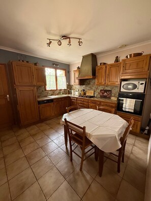 A kitchen with wooden cabinets, a tiled floor, a table with chairs, and a microwave. - Chez Polo - House with swimming pool in Vallon-Pont-d'Arc (Vallon-Pont-d'Arc)