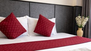 A neatly made bed with white and red bedding, a dark headboard, and a vase with flowers on the nightstand.