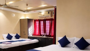 A hotel room with two beds, a wardrobe, a ceiling fan, and a window with red curtains.