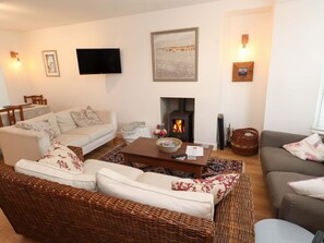 A cozy living room with a sofa, a wicker chair, a fireplace, and a television on the wall. - Bodefi (Pwllheli)