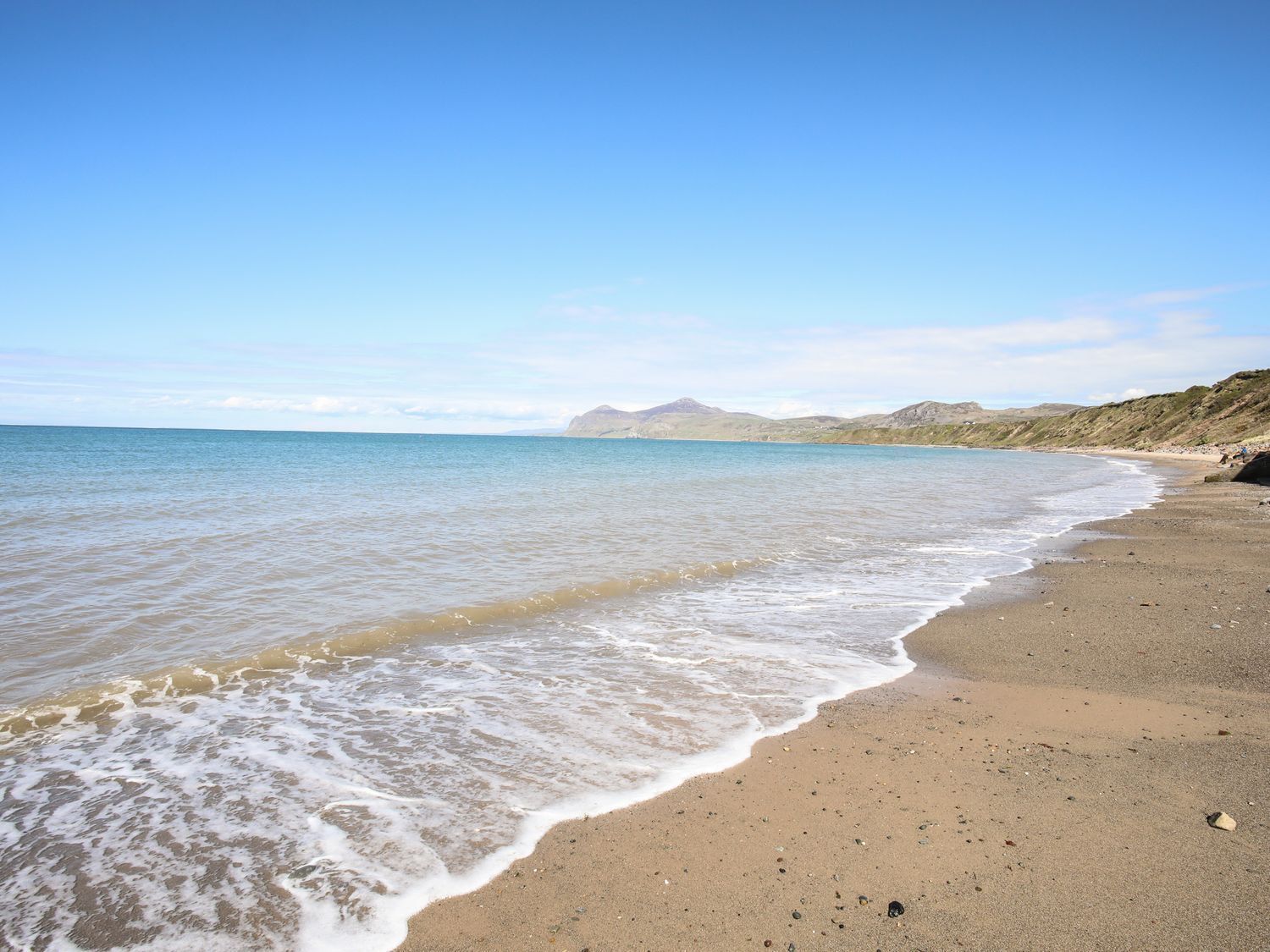 A beach with gentle waves, a clear sky, and distant hills.