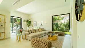 A modern living room with a sectional sofa, a tufted ottoman, a glass coffee table, and a large window offering a view of the outdoors. - Luxury villa with sea view - 10 guests (Marbella)