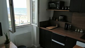 A kitchen with a view of the beach, a microwave, a coffee maker, and a trash bin. - 3 beautiful sea views (Villers-sur-Mer)