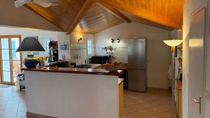 Eine Küche mit Holzbalkendecke, einer Kochinsel in der Mitte, einem Kühlschrank und einer Mikrowelle.