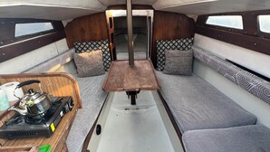 A compact interior with a central table, cushioned seating, and a small kitchenette with a kettle and stove.