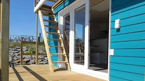 Eine Holzterrasse mit einem blauen Gebäude, einer Holzleiter und einer Steinmauer im Hintergrund.