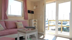 Ein gemütliches Zimmer mit einer Couch, einem Tisch und Blick auf Boote durch eine Glastür.