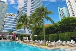 A swimming pool with lounge chairs, palm trees, and modern buildings in the background. - Luxurious 1BR Suite in Miami (Miami)