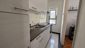 A modern kitchen with a stainless steel sink, white cabinets, and a window providing natural light. - Apartman Karlo  (Crikvenica)