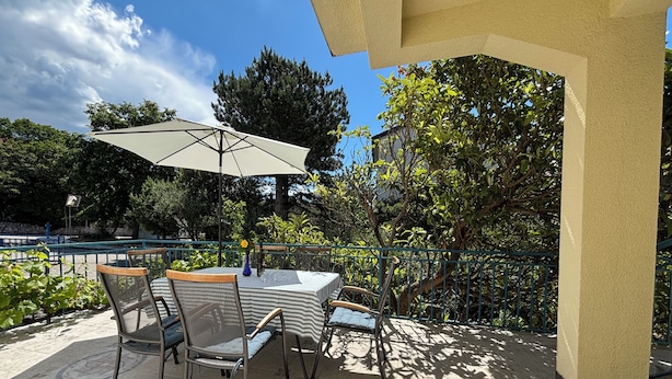A patio with a table and chairs, a pergola, and a view of trees and a pool. - Apartman Karlo  (Crikvenica)