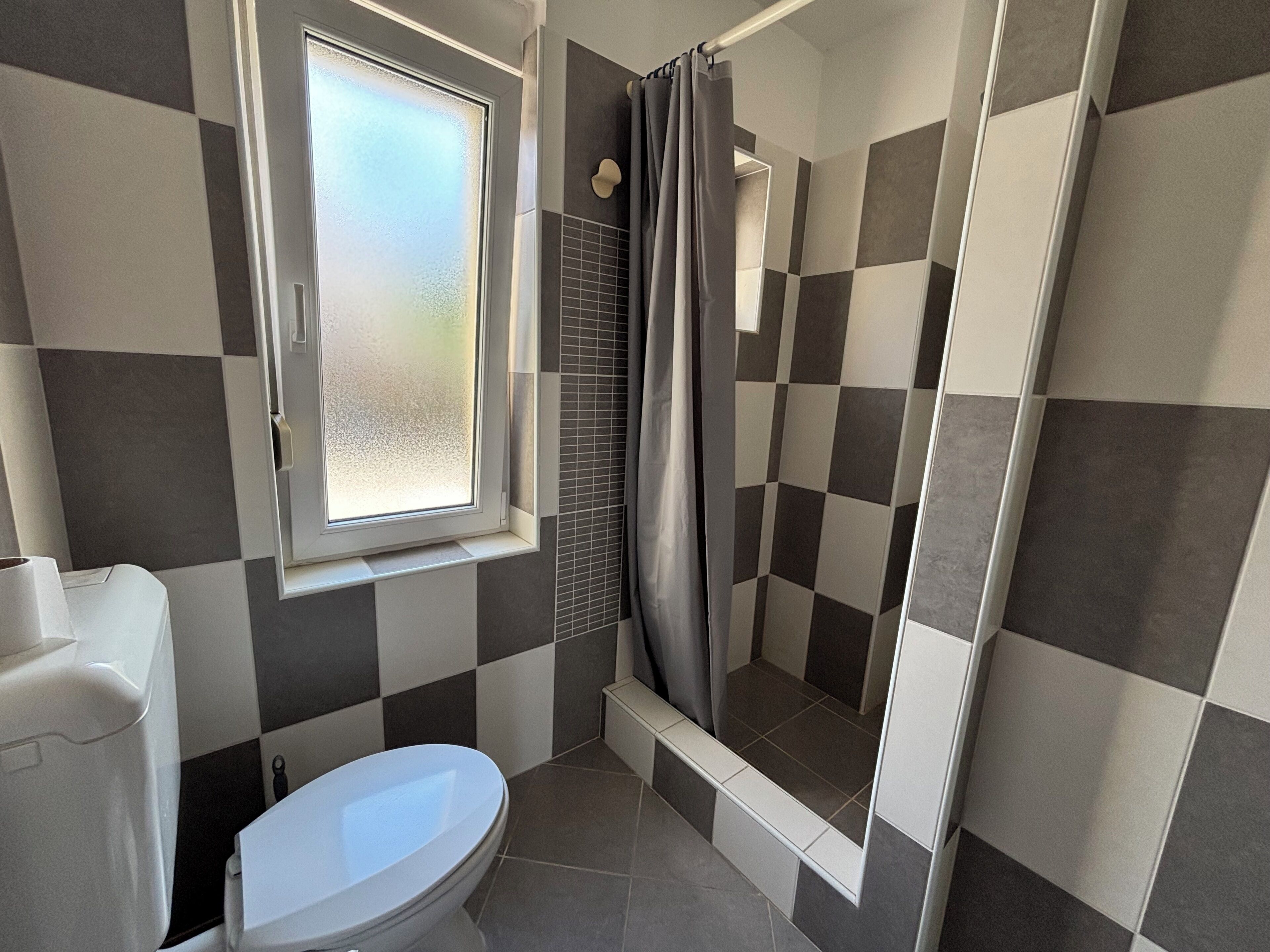 Une salle de bain avec des toilettes, une douche et une fenêtre.