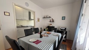 A dining area with a striped tablecloth, chairs, a bottle of wine, and a microwave. - Apartman Karlo  (Crikvenica)