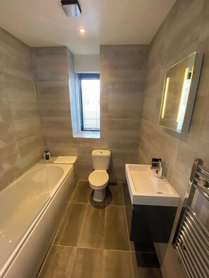 Ein modernes Badezimmer mit Badewanne, Toilette und Waschbecken, ausgestattet mit einem Fenster und einem Spiegel.