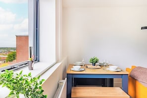 A balcony with a dining table set, a potted plant, and a view of the cityscape. - Stylish Central Location Apartment (Norwich)