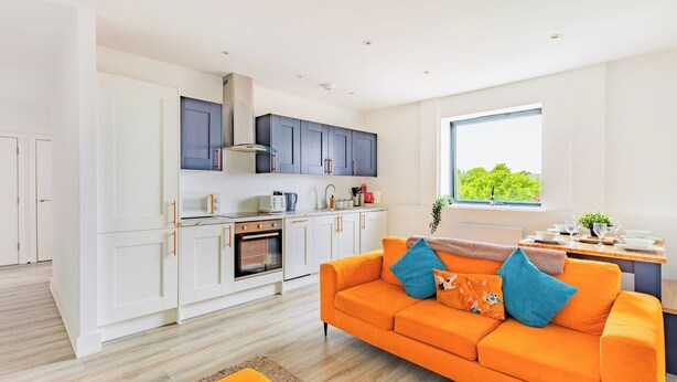 A modern kitchen with white cabinets, a built-in oven, and a window with a view of greenery. - Stylish Central Location Apartment (Norwich)