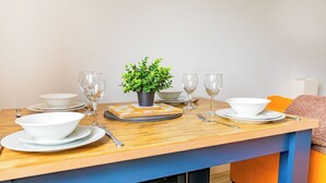 A dining table set with white bowls, plates, and cutlery, a small potted plant, and a stack of coasters. - Stylish Central Location Apartment (Norwich)