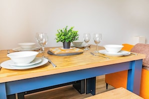 A dining table set with white bowls, plates, and cutlery, a small potted plant, and a stack of coasters. - Stylish Central Location Apartment (Norwich)