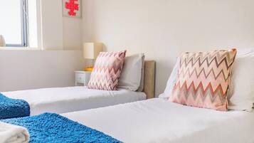 A hotel room with two beds, a nightstand, a lamp, and a window with curtains.