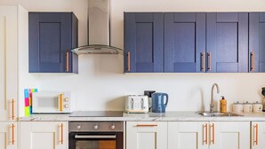 A kitchen with white cabinets, a microwave, a toaster, a kettle, and a sink. - Stylish Central Location Apartment (Norwich)
