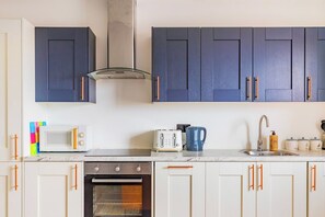 A kitchen with white cabinets, a microwave, a toaster, a kettle, and a sink. - Stylish Central Location Apartment (Norwich)