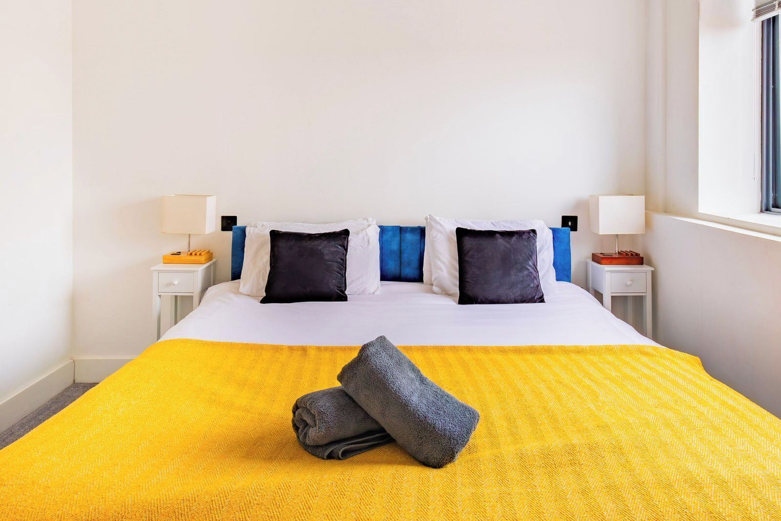 Een hotelkamer met een bed, twee nachtkastjes, een raam en een gele sprei.