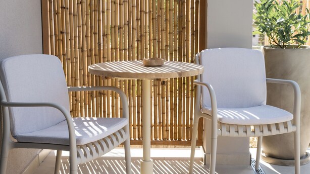 A patio with two white chairs and a round table, a bamboo screen, and a potted plant. - Seagonia (Aktio-Vonitsa)