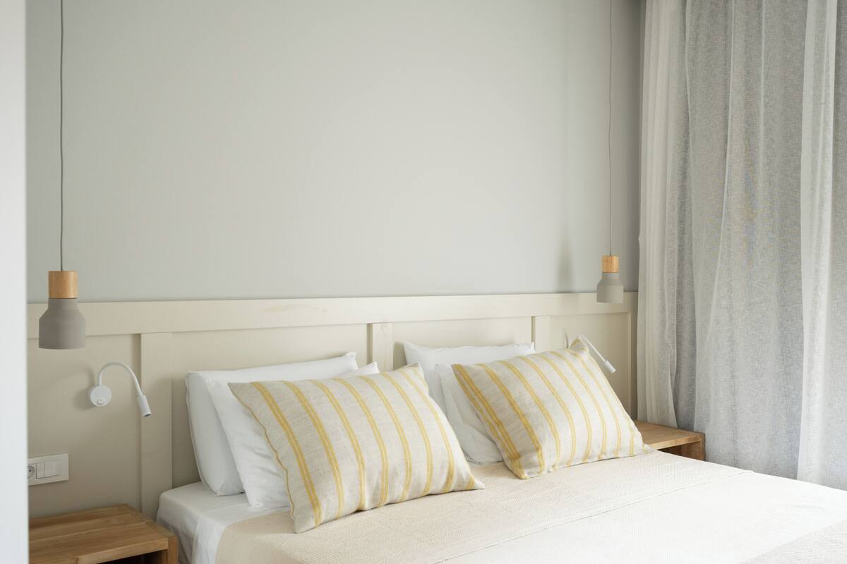 A bedroom with a bed, two bedside tables, a nightstand, a wall-mounted lamp, and a curtain.