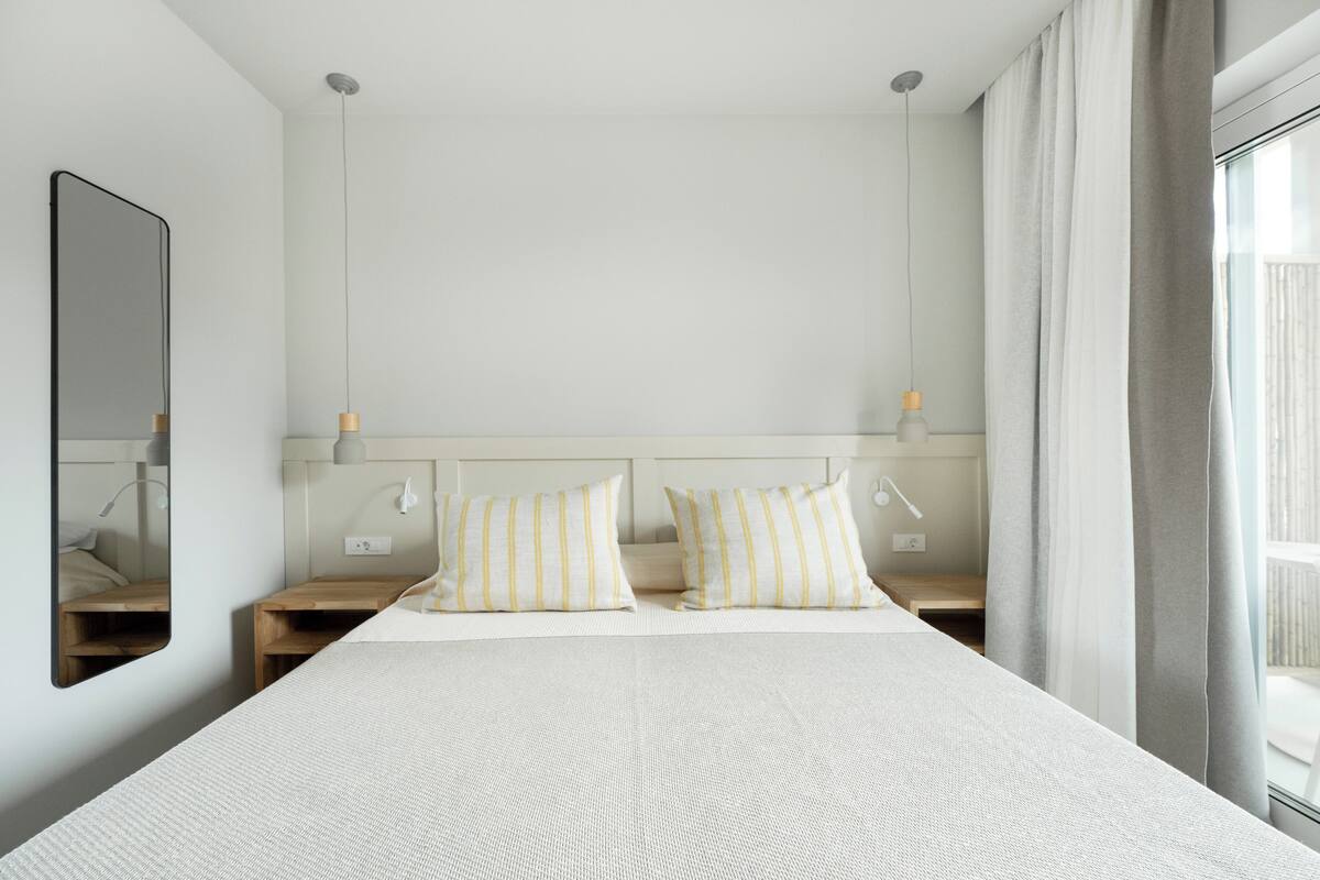 A neatly arranged hotel room with a large bed, two bedside tables, a mirror, and a window with curtains.