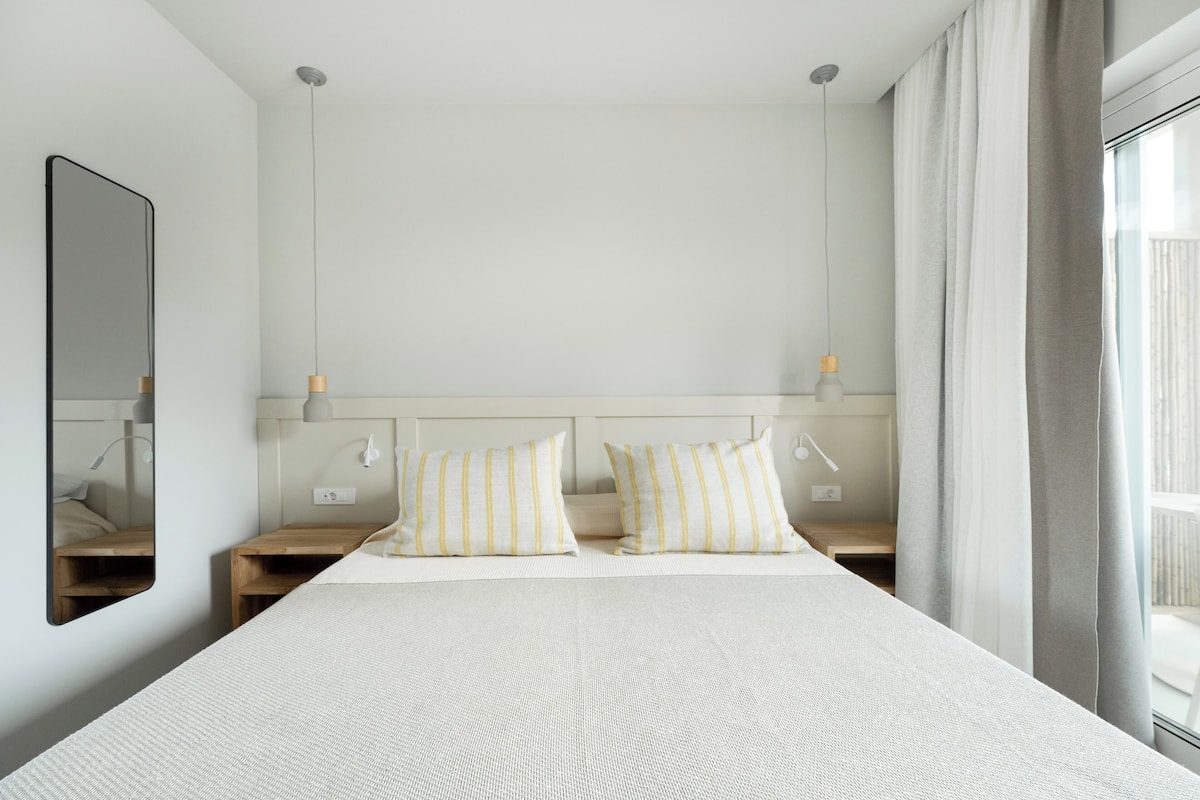 A neatly arranged hotel room with a large bed, two bedside tables, a mirror, and a window with curtains.