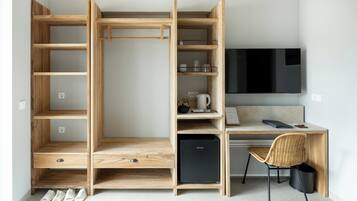A compact room with a built-in desk, a small black refrigerator, a wicker chair, and a TV mounted on the wall.