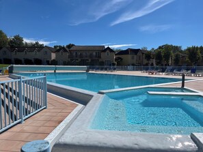 Ein Swimmingpool mit gefliestem Sonnendeck, Liegestühlen und einem weißen Zaun.