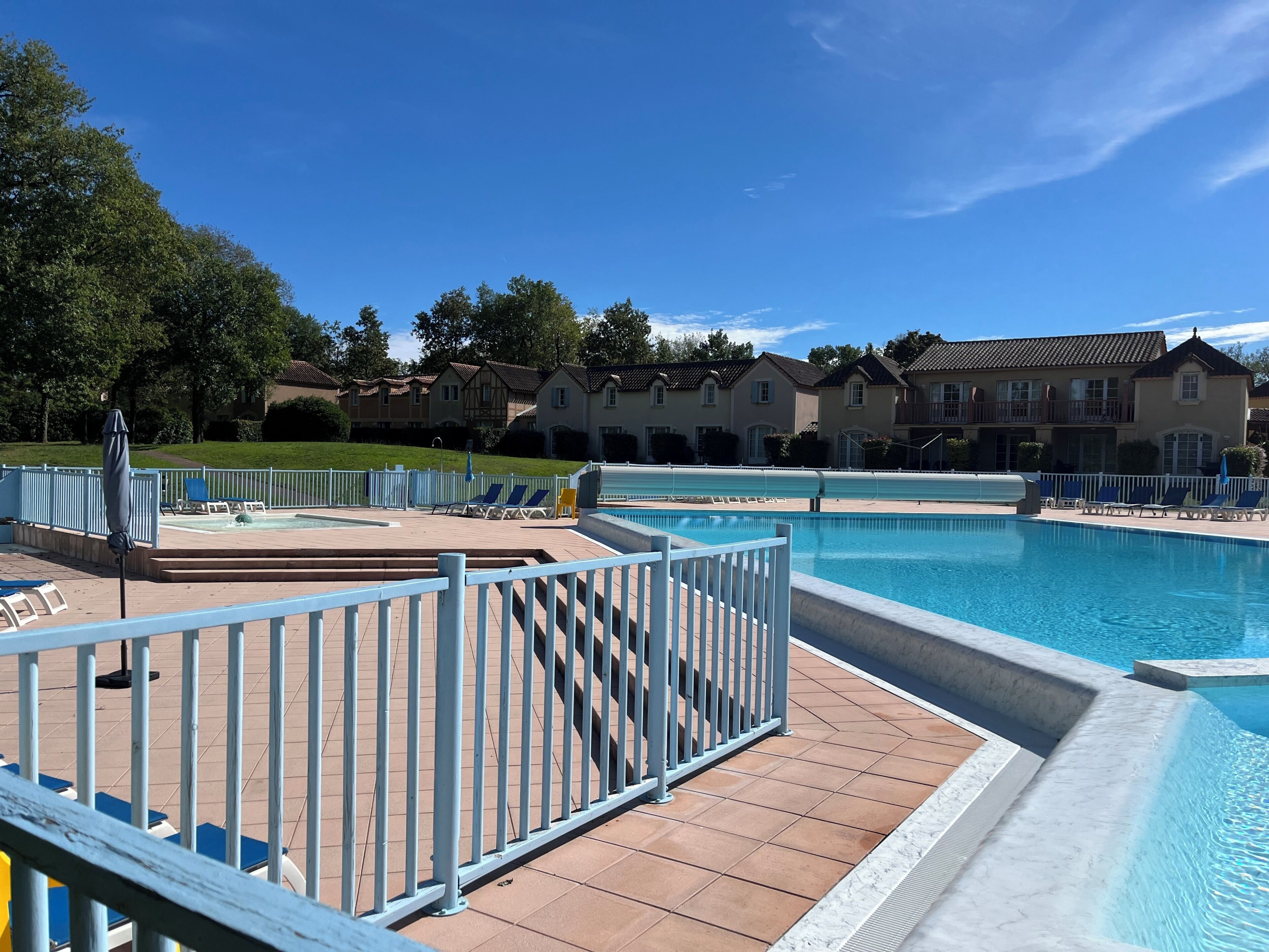 A swimming pool with a tiled deck, lounge chairs, and a fence.
